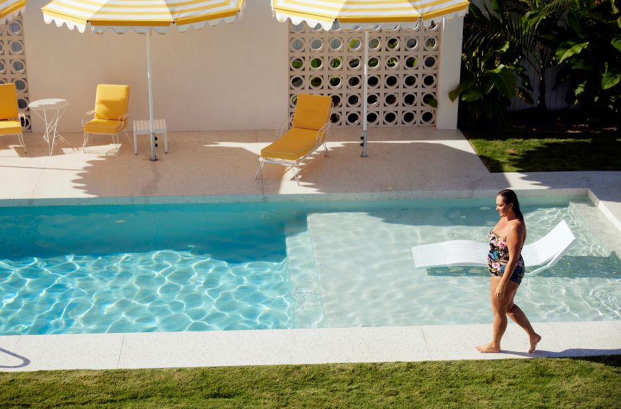 Woman with brown hair walks along the side of the Palm Springs inspired pool 