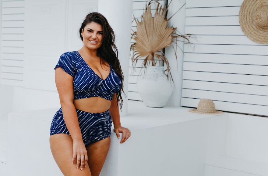 Woman with long brown hair wears navy and white polkadots crop wrap top and retro style high waisted pants