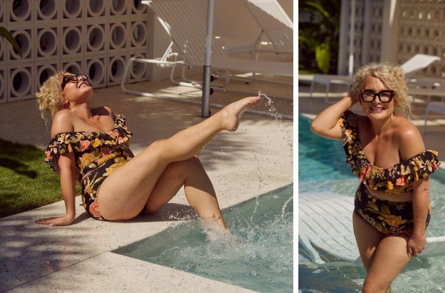 Woman with short curly blonde hair poses in the pool wearing black and floral off the shoulder bikini top and high waisted pants