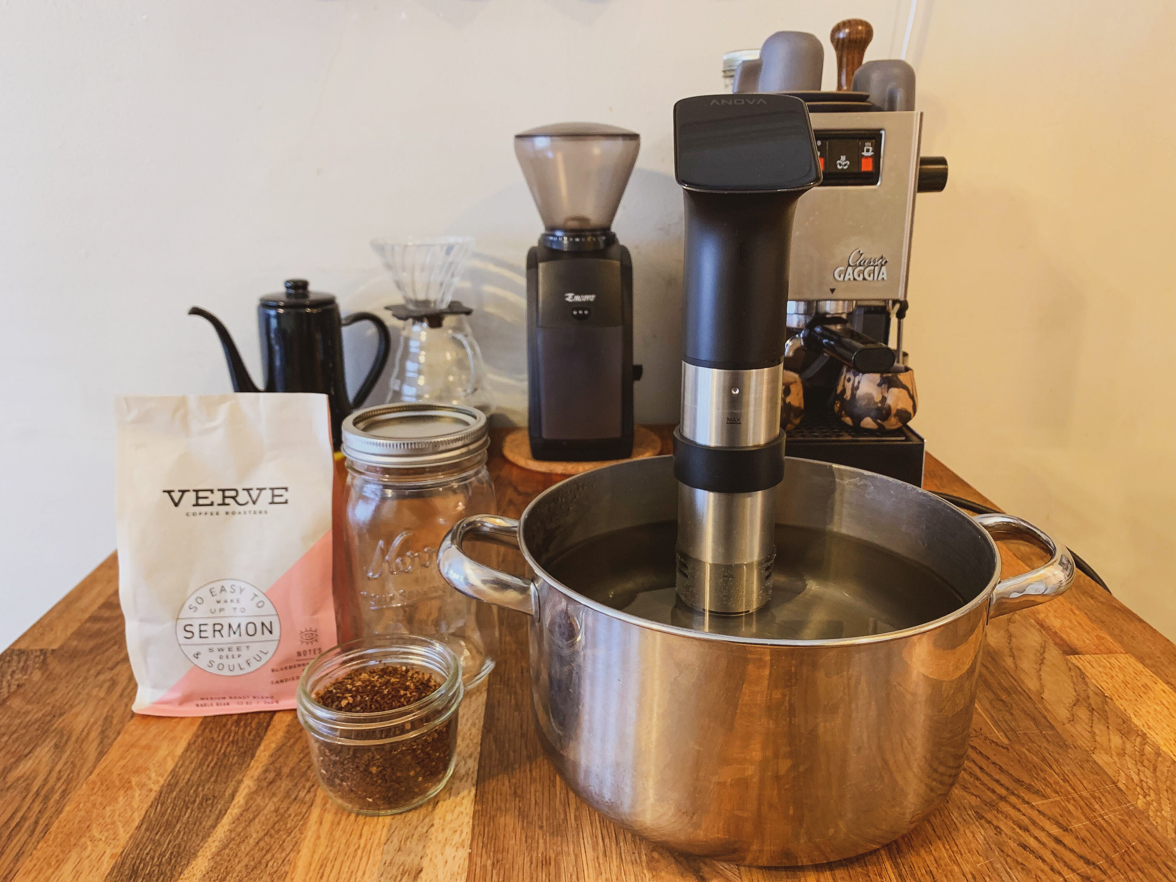 The Anova Precision Cooker Pro sous vide circulator in a pot of water along with other accessories and ground coffee to make cold brew.