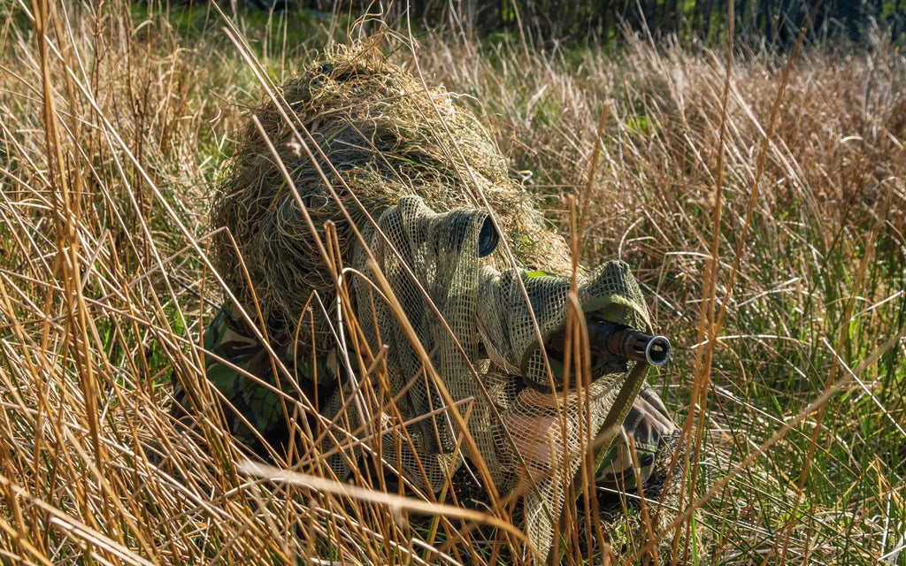 Franco-atirador camuflado na relva com fato de camuflagem ghillie