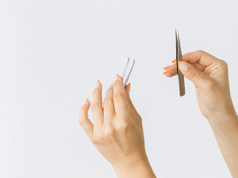 A person holding up a fine point tool that can be used to unknot jewelry or necklace chains.