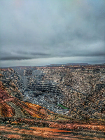 A large whole in the earth caused by natural diamond mining practices, with a gloomy sky background.