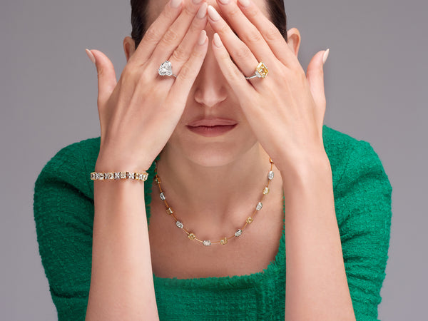 Woman covering eyes with fancy yellow diamond rings, bracelet, and necklace.