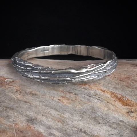 Oxidised sterling silver bangle by Kara Jewellery on a log with a black background.
