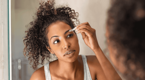 Black woman applying hydrating oil to eyebrows to treat dandruff.