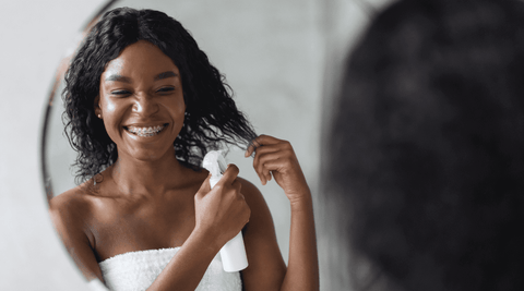 Black woman moisturizing hair to prepare for DIY shea butter mask. 