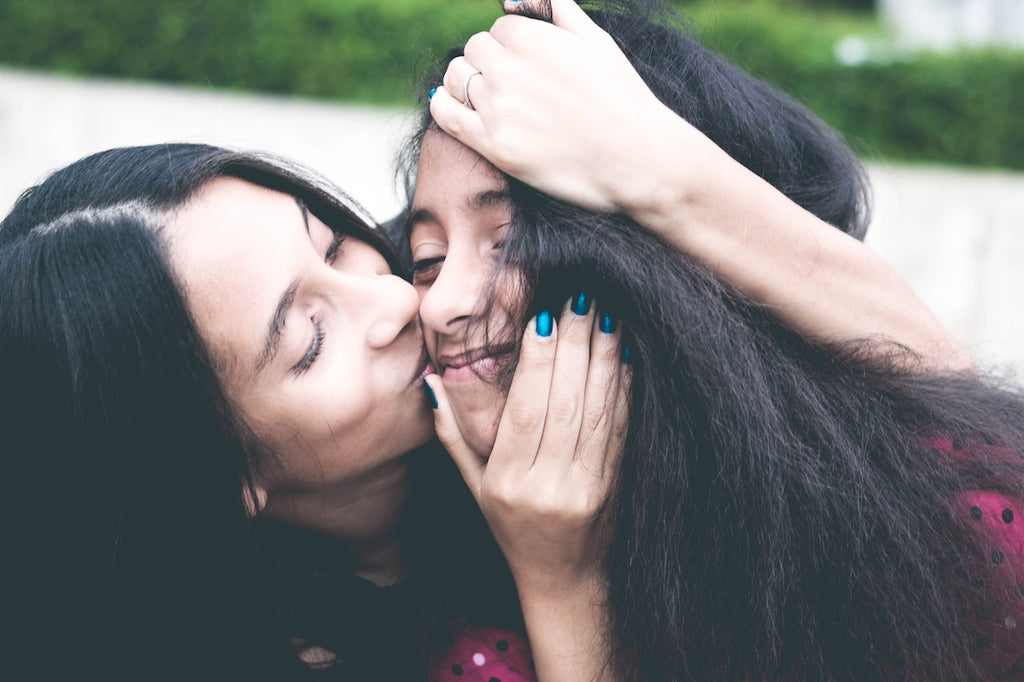 Image of woman kissing another woman on the cheek in a friendly embrace