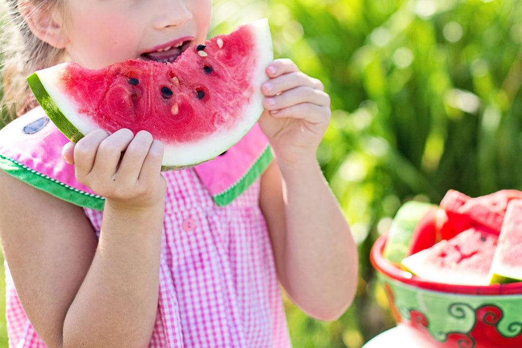 Girl wearing a pink shirt biting into a large slice of watermelon