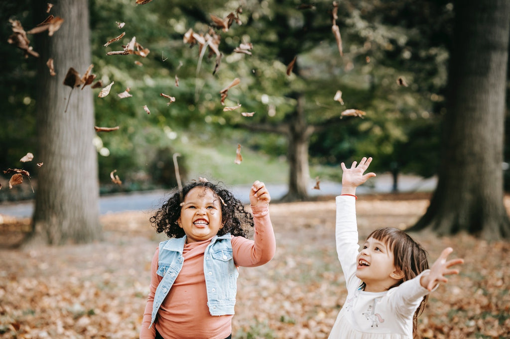 Image of two young girls playing and throwing leaves in the air during fall