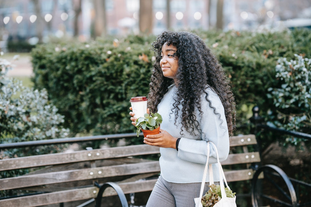 Image of woman holding a coffee and a plant walking outside