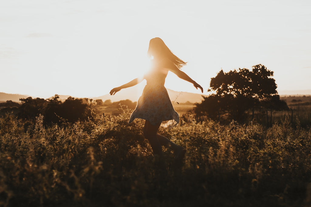 Image of woman running through a field during sunset