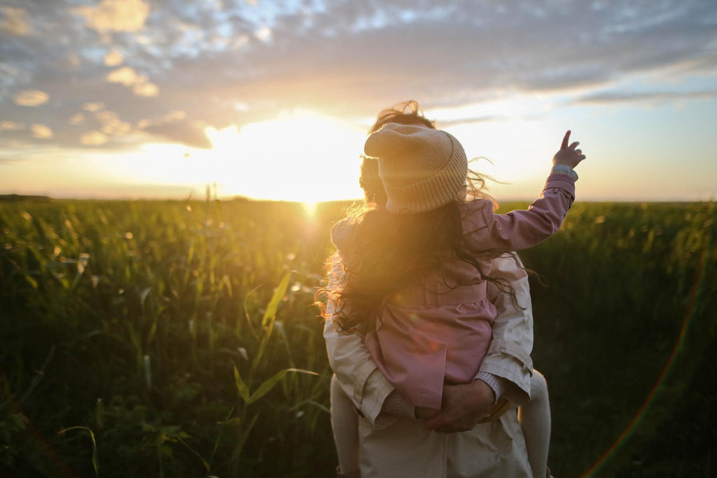 Image of parent holding young kid in an open green space while the sun sets