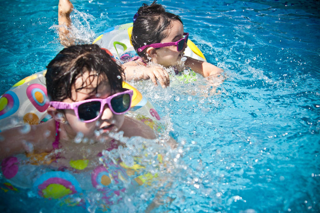 Two kids wearing goggles and swimming with floaties in water