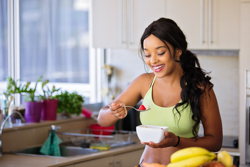 Woman eating a yogurt and fruit bowl sitting at a kitchen table