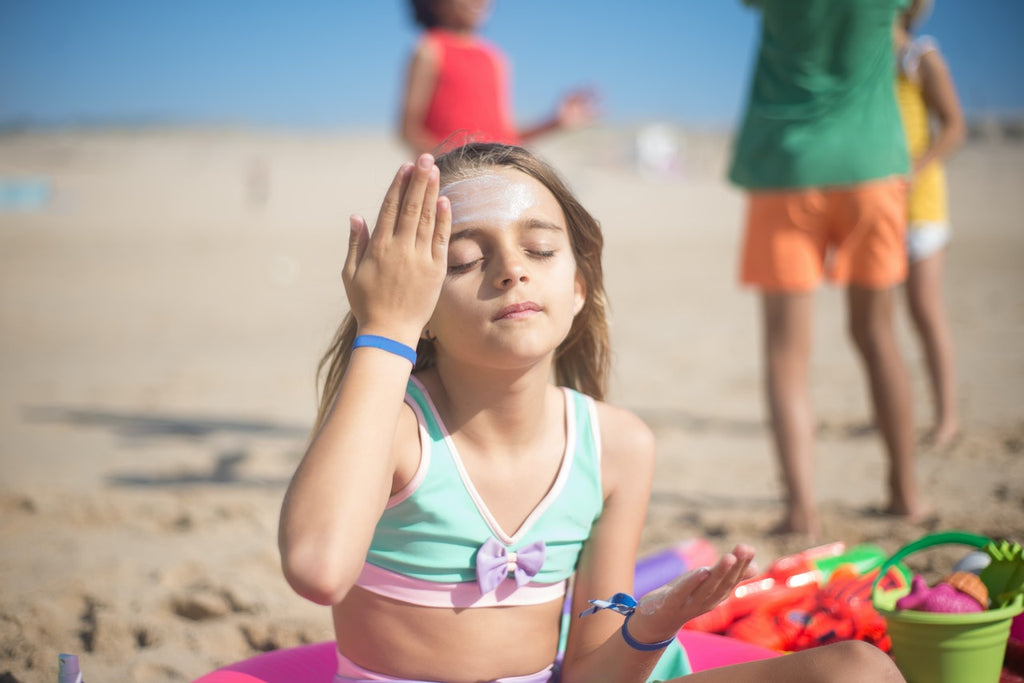 Young girl applying sunscreen to her forehead at the beach