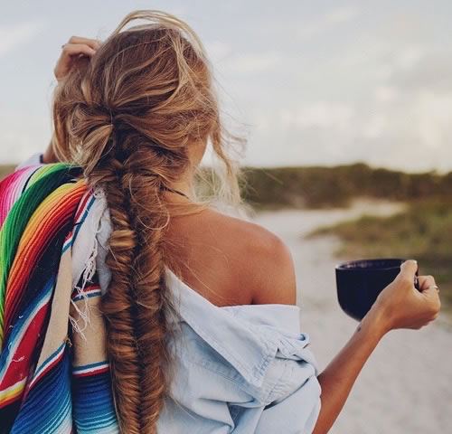 Woman with braided hair on beach with mug in her hand