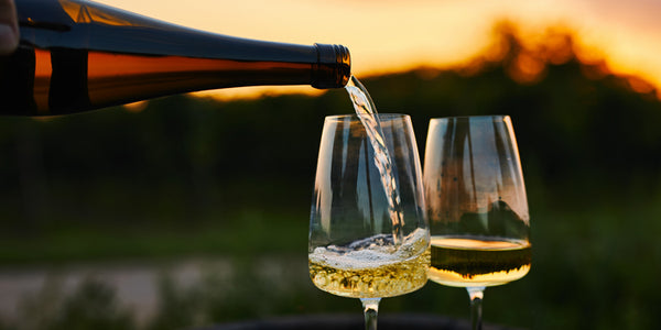 Pouring Rielsing white wine into glasses in the vineyard at sunset