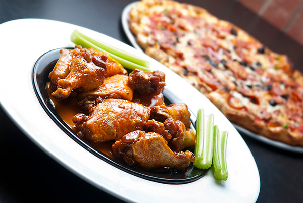 chicken wings on a plate with pizza in the background