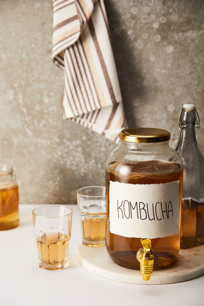 A jar of kombucha with two glasses on the white table