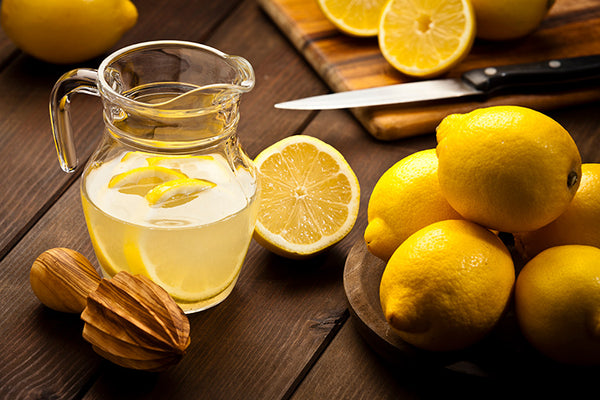 A jug with infused lemon water and fresh organic lemons on rustic wood table