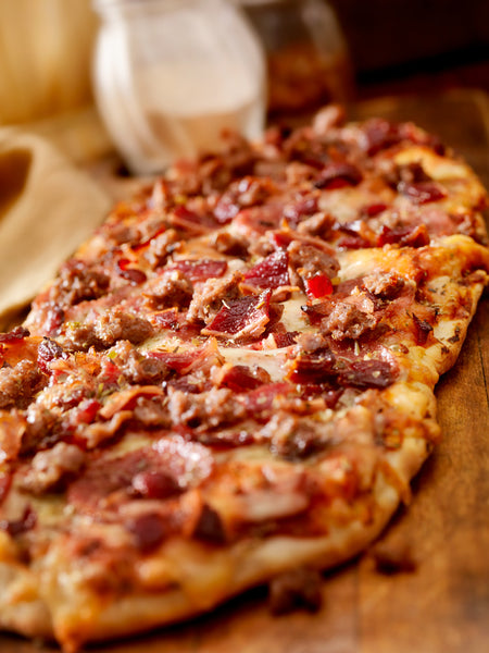 Freshly baked flatbread pizza with fennel sausage, pepperoni and uncured bacon on a wooden table