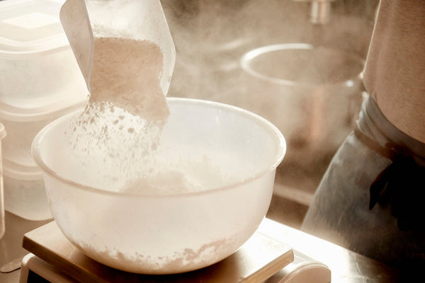 A baker preparing ingredients, using a measuring scale and pouring flour into a bowl