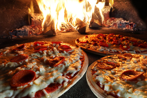 Three pizzas are baked in a pizza oven on firewood.