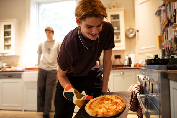 A young man is getting homemade pizza out of the oven.