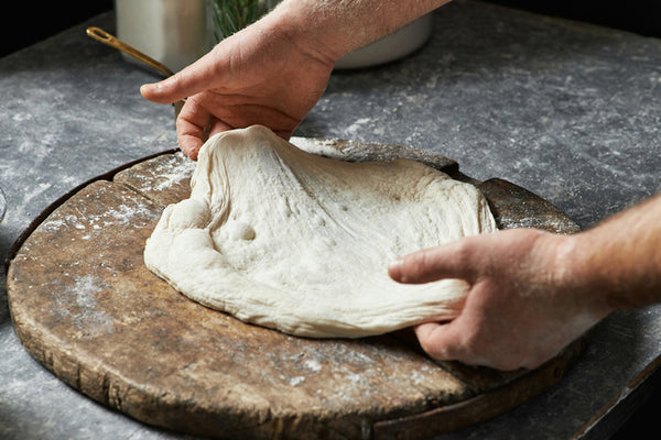 Hands of a chef preparing pizza dough on a wooden tray