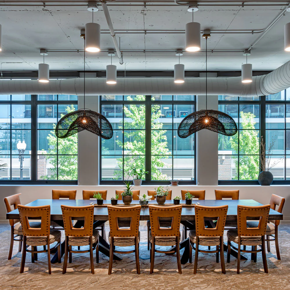 Large conference room with wood look concrete table surrounded by modern chairs and pendant lights overhead.