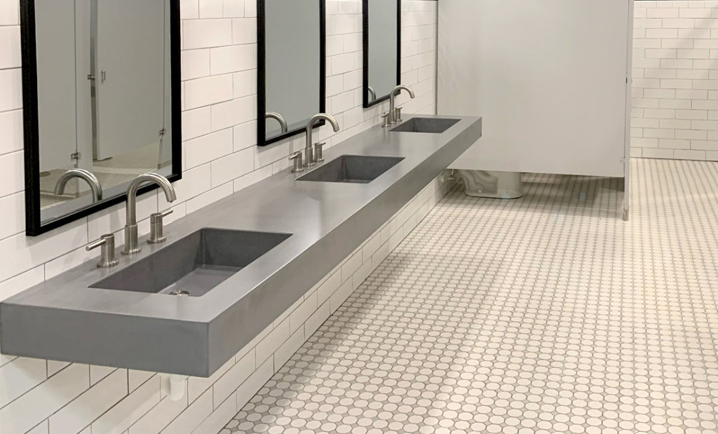 Triple station concrete sink in a commercial bathroom with white backsplash tile.