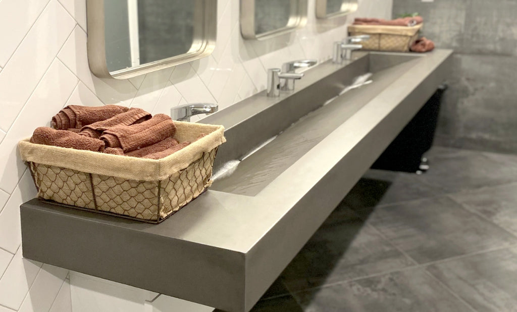 Long concrete trough sink in a commercial bathroom with three faucets.