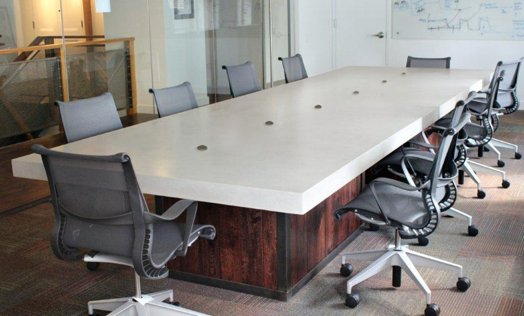 Large conference table in concrete with wood base and wheeled chairs surrounding it.