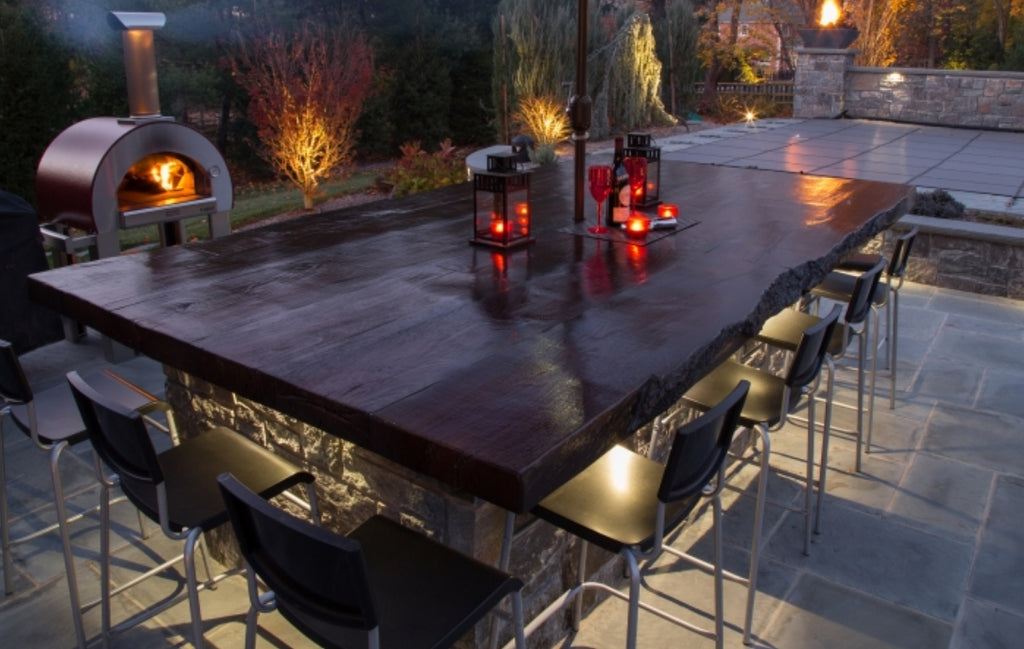 Large dining table in wood look concrete placed outdoors with chairs surrounding it.