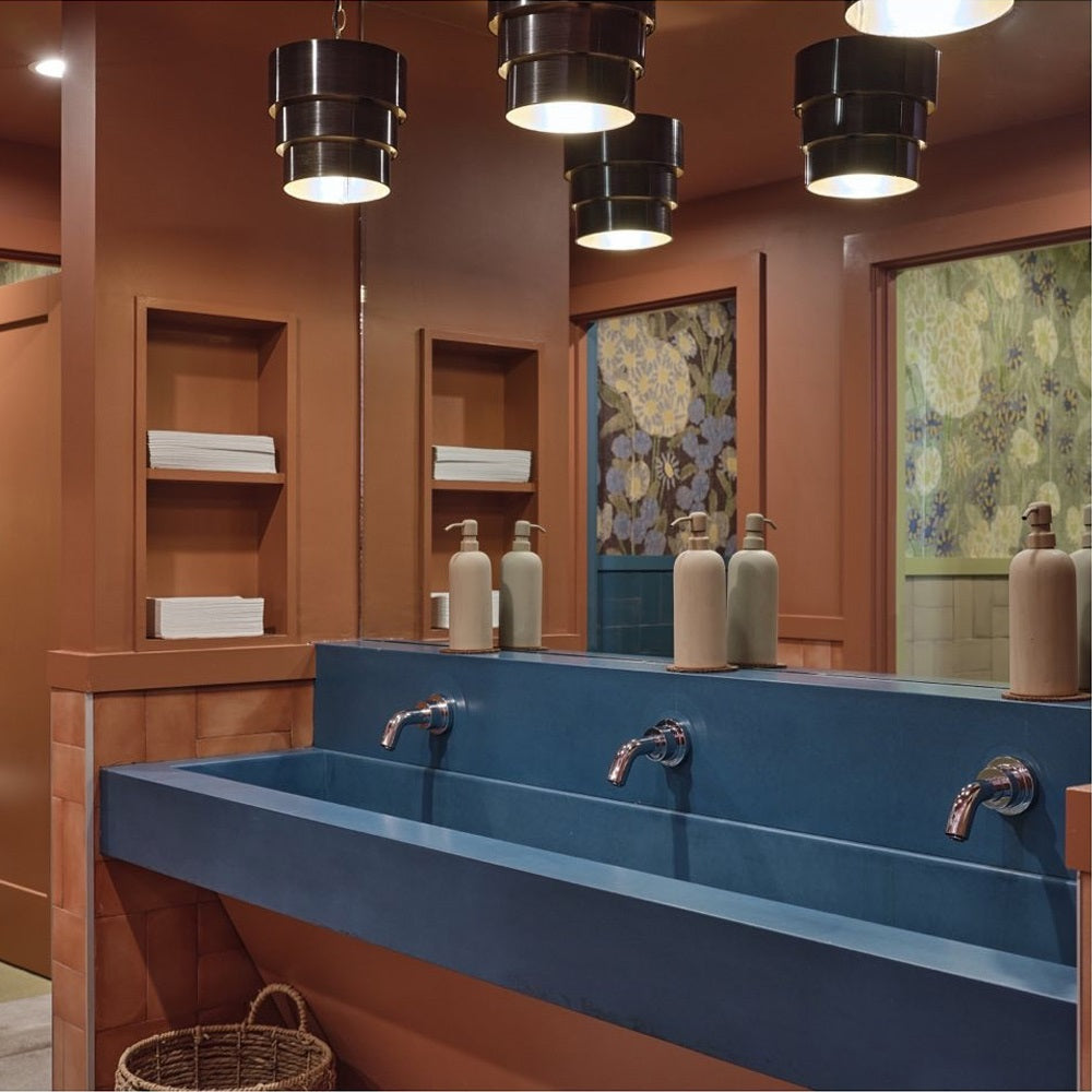 Bathroom covered in rich woods with a blue concrete triple sink with spout faucets.