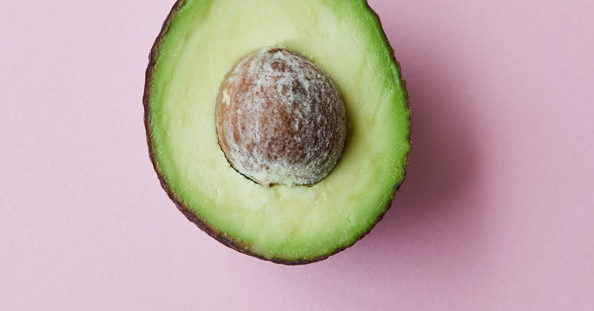 Pink countertop with half an avocado viewed from the top.