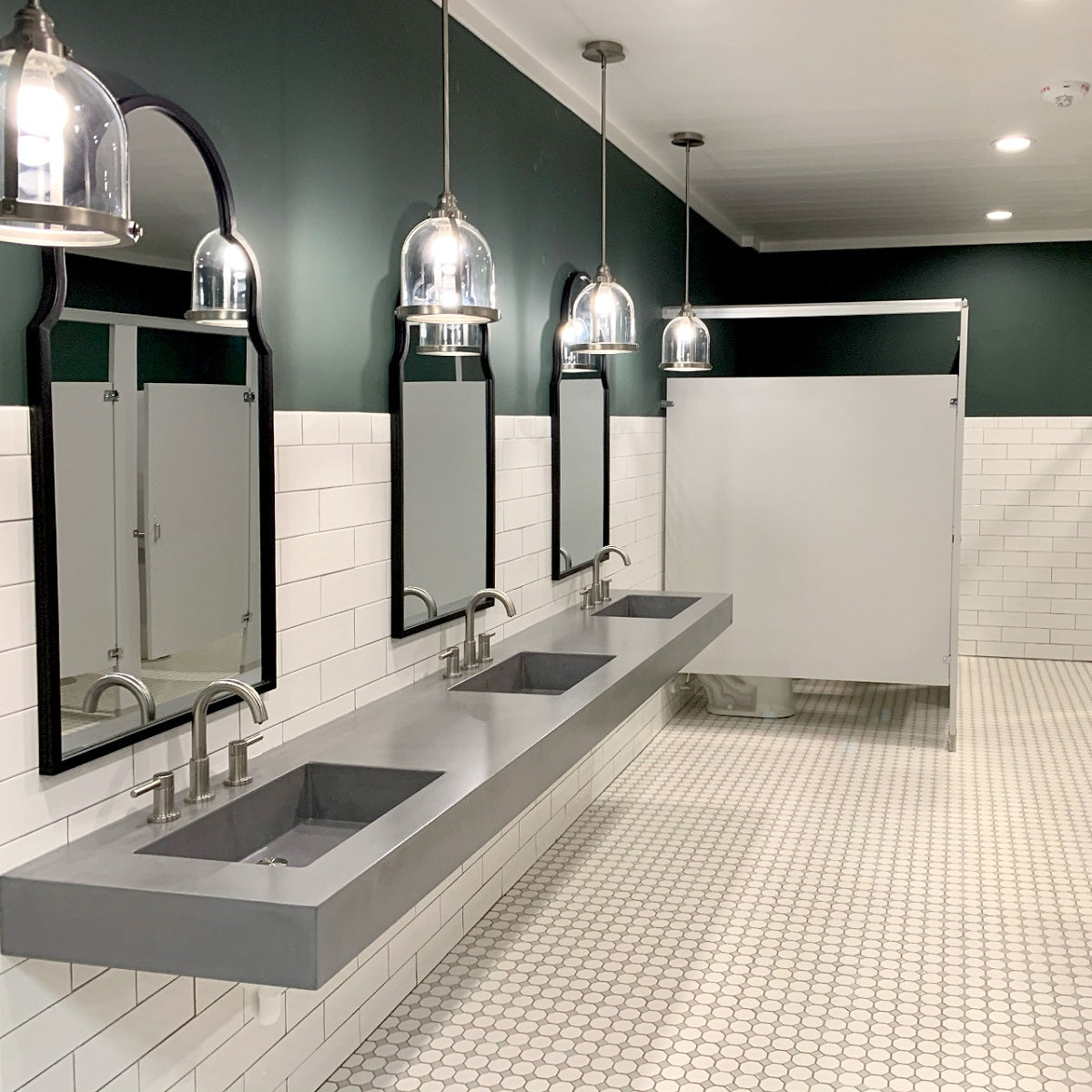 Commercial bathroom with gray concrete sinks and marble flooring and tile backsplash.