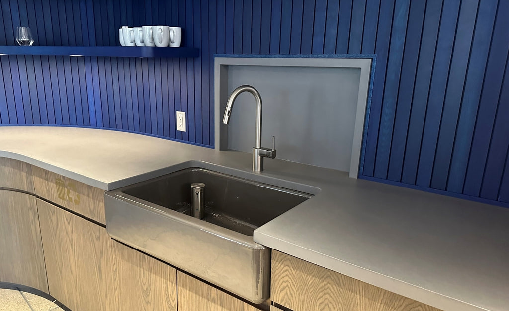 Simple kitchen with light concrete countertop and a farmhouse sink with blue slat backsplash.