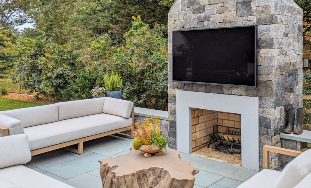 Concrete fireplace on an outdoor patio with cushy seating and television.