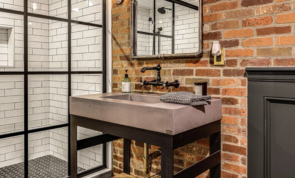 Single user commercial bathroom in an industrial style including brick walls and concrete console sink.