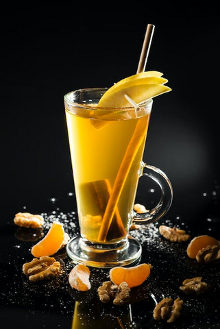 A close-up of a glass of hot toddy garnished with lemon skin and cinnamon sticks against a dark backdrop