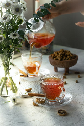 A cup of warm tea and cider punch and a person pouring it from a crystal kettle into another cup