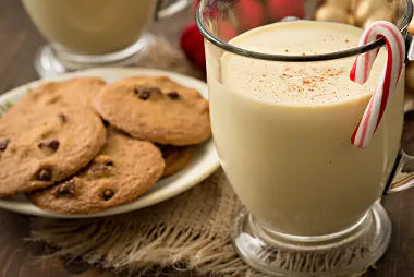 A glass of peppermint eggnog garnished with candy cane and a plate of chocolate chip cookies