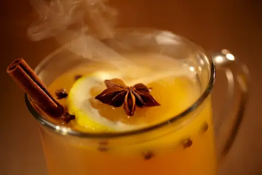 A steaming cup of woodchuck warmer apple cider garnished with cloves, cinnamon stick, lemon wheel and a star anise pod