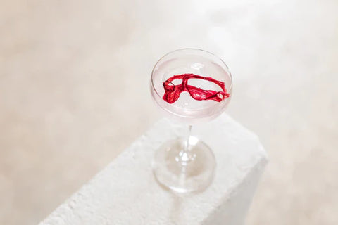 Alcohol free rhubarb gimlet cocktail in a small wine glass garnished with dried rhubarb displayed on a white wall