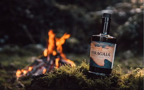 bottle of Feragaia displayed on a mossy foreground with a log fire in the background