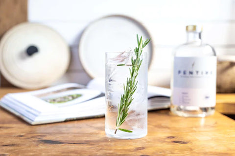 Glass of Pentire Adrift & Tonic alcohol free displayed in front of a bottle of non-alcoholic Pentire adrift and a cookery book on a wooden work surface