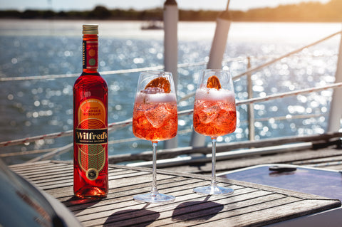 Wilfred's Aperitif Pictured on a table beside two glasses with a view out to sea with the sun glinting off the water.  