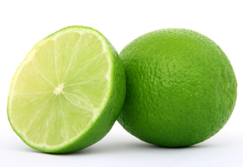 One whole lime displayed next to half a lime cut up ready to go into an alcohol free gimlet cocktail displayed against a white backgroun